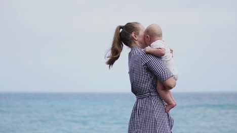 against the backdrop of the ocean, the mother lifts her son high in the air, their playfulness enhancing the seaside atmosphere. a young family's joy is evident