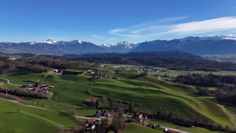 the glarner alps shadowing jona village in switzerland, lush green fields under clear blue sky, aerial view