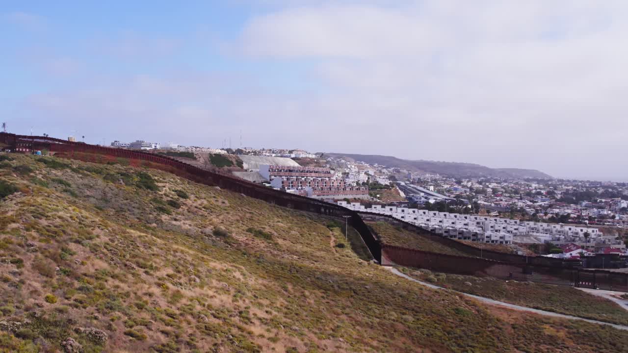 Drone footage captures a wide shot of the border wall as it snakes through rugged terrain and separates Tijuana from southern California.