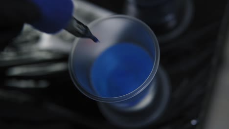 tattoo master merges ink into water from a tattoo machine. black safety gloves, female master artist cleans blue ink needle pouring it into water. top view. close up