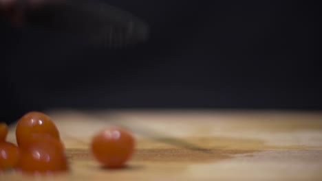 Close-up-shot-of-someone-cutting-cherry-grape-tomatoes-on-cutting-board-with-black-background