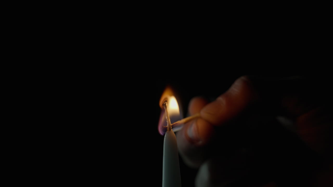 Gros plan d’une main tenant une allumette allumant une bougie sur un fond sombre. Flamme vive