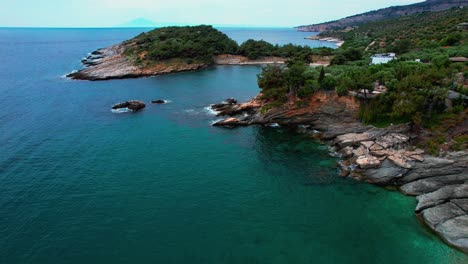 cinematic aerial reveal of a secluded beach with turquoise waters, cliffside houses and lush greenery, aliki beach, thassos island, greece