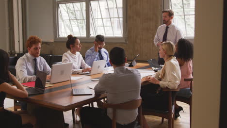 Middle-aged-businessman-leading-a-meeting,-seen-from-doorway