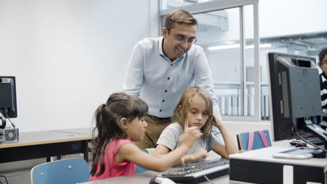 niñas multiétnicas escribiendo en el teclado mientras un profesor masculino las observa
