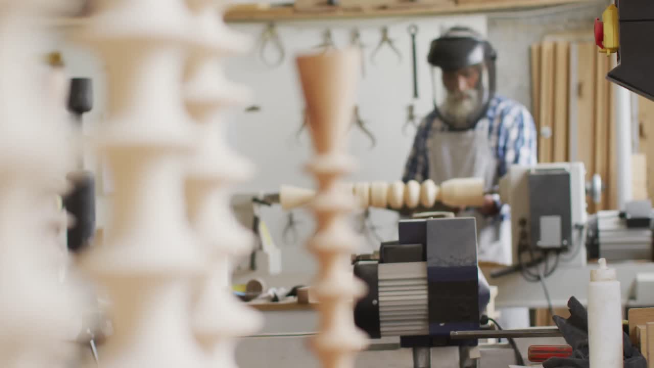 African american male carpenter wearing protective helmet turning wood on a lathe at carpentry shop