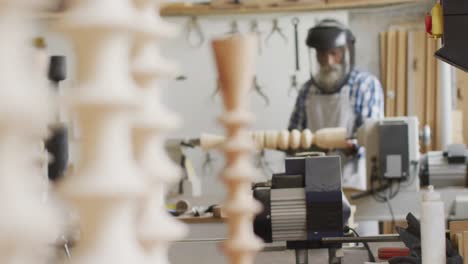 african american male carpenter wearing protective helmet turning wood on a lathe at carpentry shop