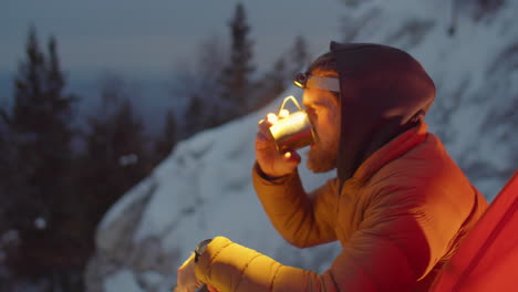 tourist sitting by camping tent and drinking hot tea in evening