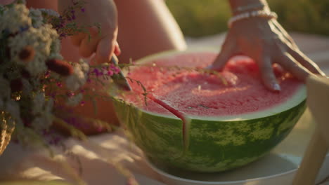 close-up of a hand firmly holding a juicy, red watermelon while slicing through its vibrant flesh, fresh, green rind contrasts with pink interior as individual cuts the fruit