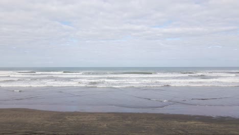 Vuelo-Aéreo-Hacia-Atrás-Que-Revela-Un-Vehículo-4wd-Conduciendo-A-Lo-Largo-De-Una-Playa-Y-Un-Hombre-Parado-En-Las-Dunas