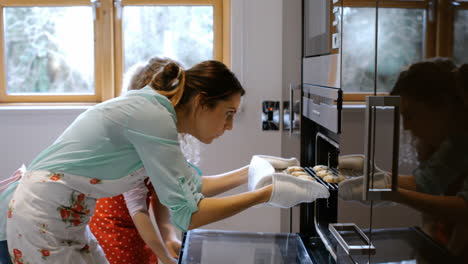 mother and daughter are putting cakes in the oven