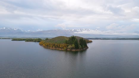 vuelo de drones sobre una isla exuberante en un lago y los alpes del sur de nueva zelanda en el fondo