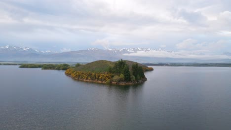 drone flight over lush island on a lake and southern alps of new zealand in background