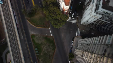 The-drone-circles-over-the-road-and-descends-to-the-intersection,-a-train-passes-by,-cars-drive-by,-a-sunny-day