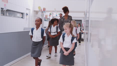 teacher and pupils walking along corridor in busy elementary school corridor