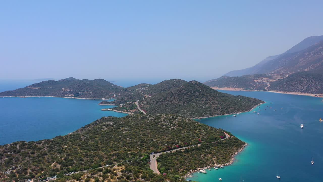 Aerial drone panning left across a peninsula full of large green hills in Kas Turkey and anchored boats in the blue tropical sea of the Mediterranean on a sunny summer day