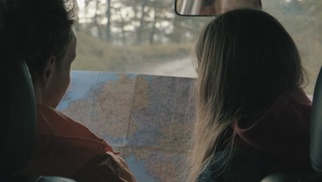 young male and female looking at a map inside a car