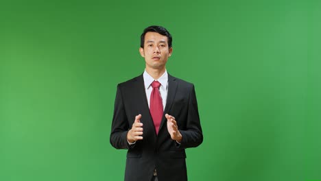 young asian businessman in suit jacket standing and presenting something on green screen background, chroma key