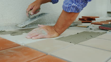 a man is laying tiles on the floor only hands are visible in the frame