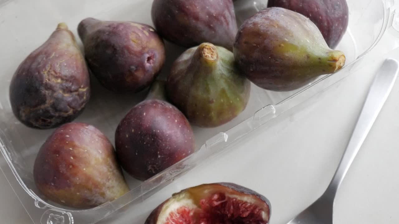 Fichi freschi in un contenitore trasparente, primo piano, che evidenzia la loro buccia viola e la forma unica.