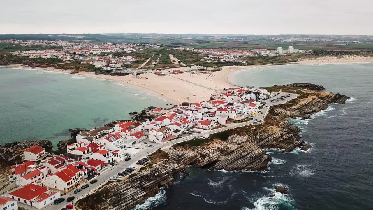 A scenic aerial view of Baleal, Portugal, featuring its coastal village with red-roofed houses, rugged cliffs, and sandy beaches surrounded by the Atlantic Ocean and a vibrant coastal landscape
