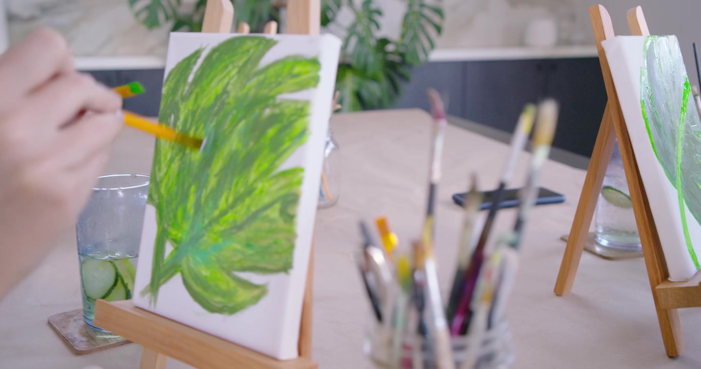 Pintoras diversas en un estudio, mojando el pincel y mezclando verde en la paleta, pintando una hoja grande.