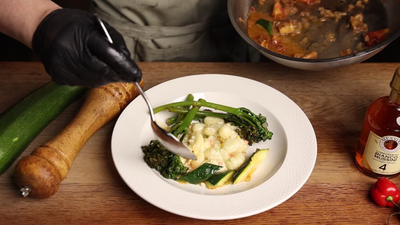 Chef Plating Gnocchi with Broccoli and Zucchini on a White Plate