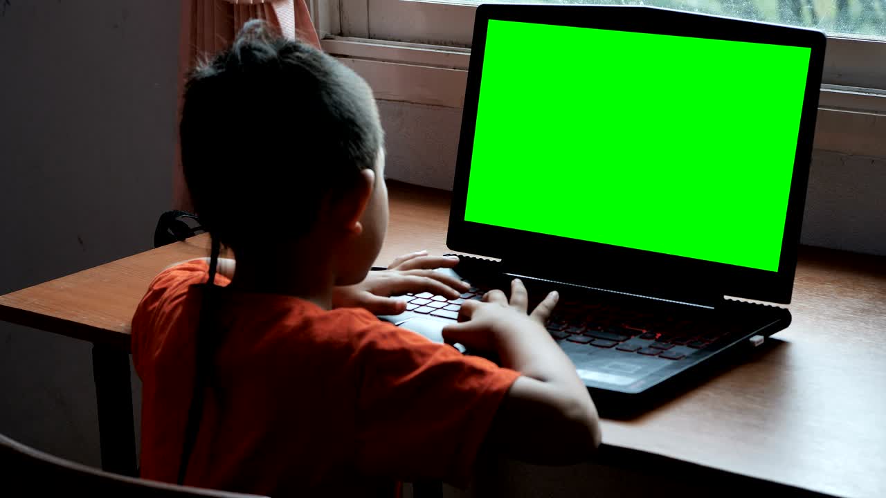 niño asiático de 7 años usando portátil busca información en internet en casa con pantalla verde. concepto de tecnología en la vida cotidiana.