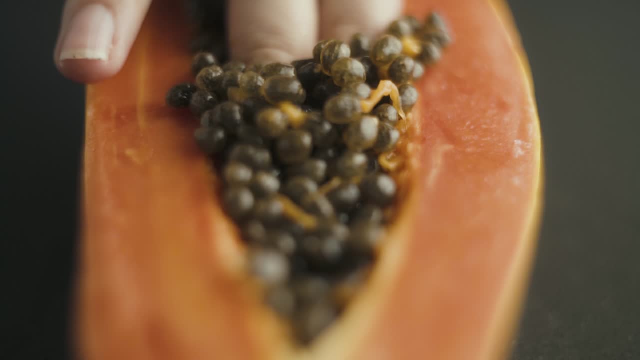 cerca de dedos femeninos sumergiéndose en las semillas de papaya cortadas por la mitad