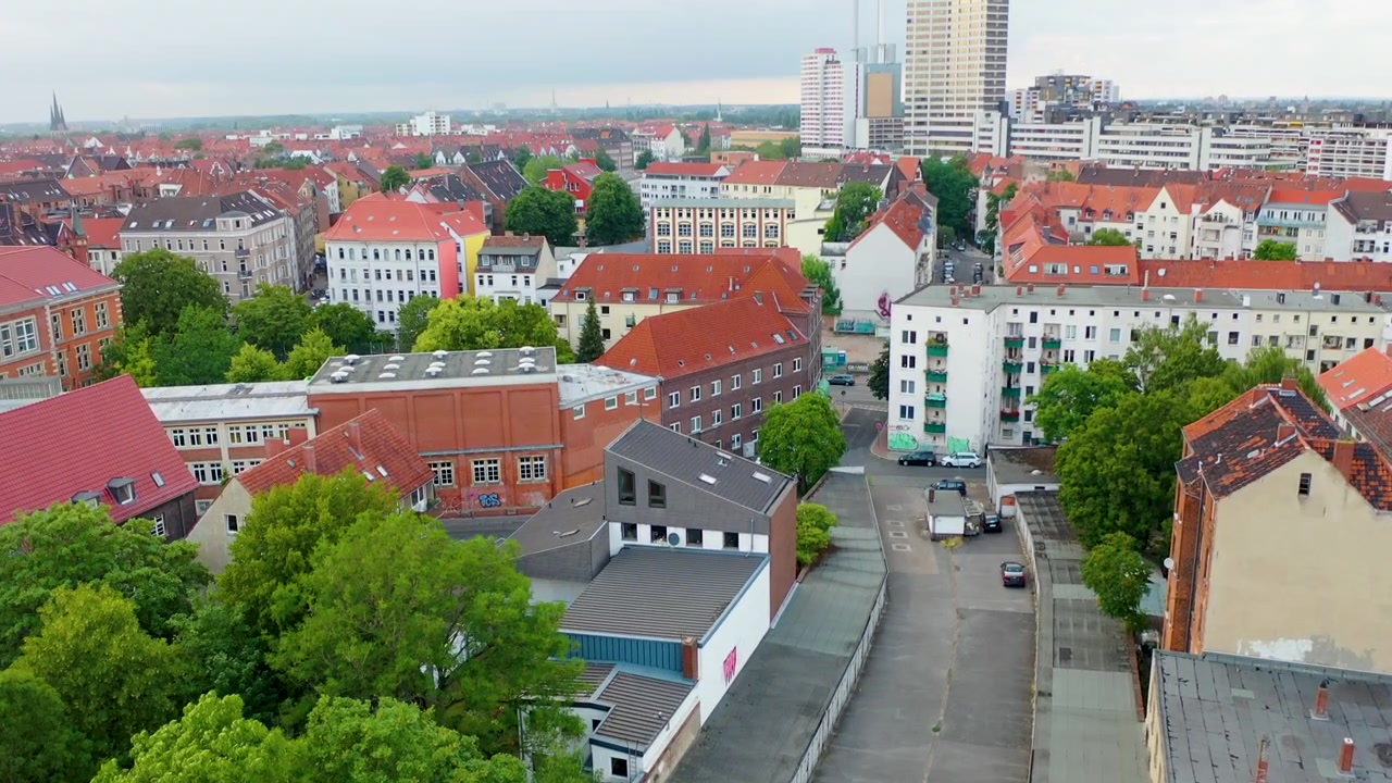 Ripresa aerea cinematografica che si eleva lentamente sopra edifici residenziali, rivelando un vivace paesaggio urbano ad Hannover, Germania.