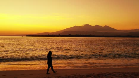 silhouette de fille marchant seule sur une plage de sable après le coucher du soleil avec un beau ciel jaune coloré reflétant sur l'eau de mer vibrante au myanmar