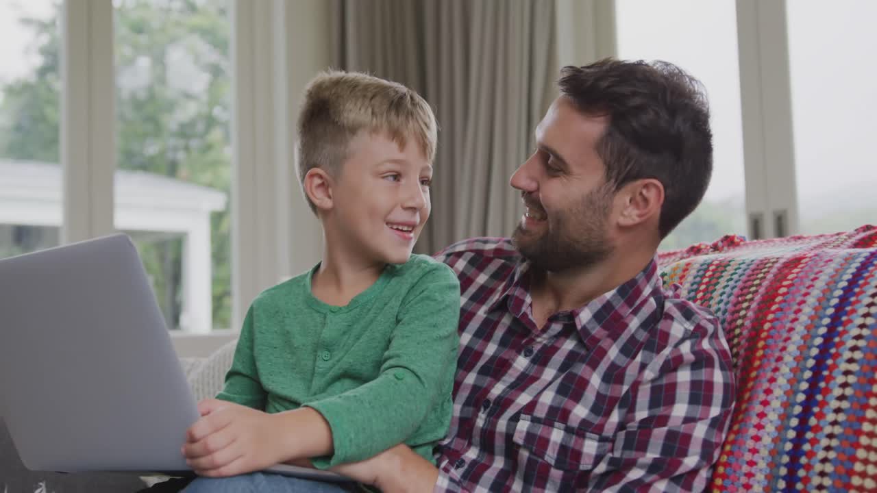 padre e hijo usando una computadora portátil en un sofá en un cómodo hogar 4k
