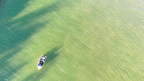 drone captures a boat navigating tranquil, clear waters with shifting shadows and sunlight