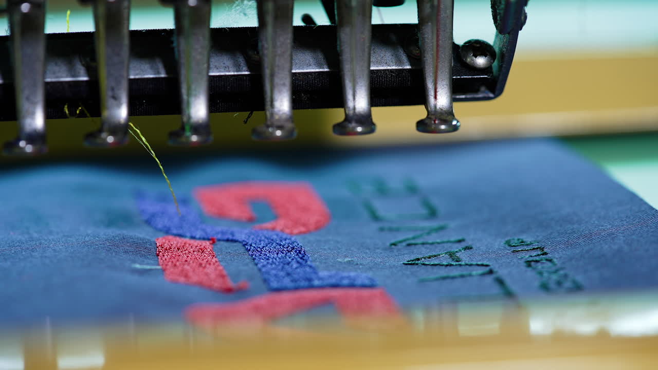 Dressmaking machine making a thread stitches. Work of automated embroidery machine on blue cloth. Sewing needle moving rapidly on fabric. Close-up.