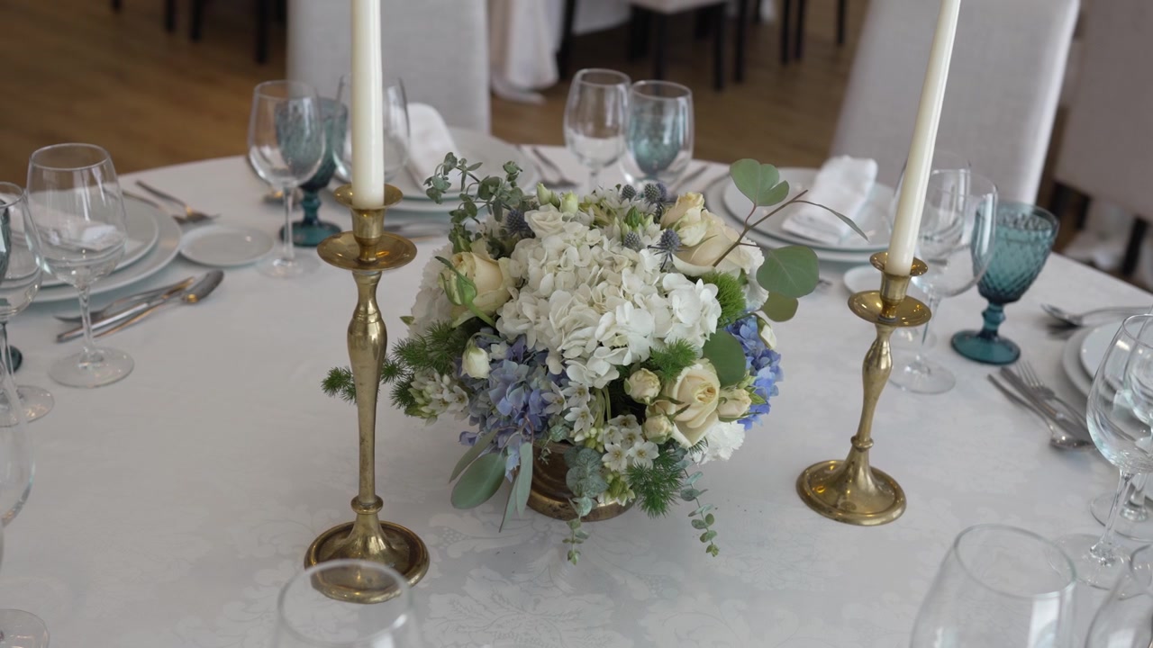 Elegant borddekorasjon med hvite og blå blomster, gulllysestaker og fint servise