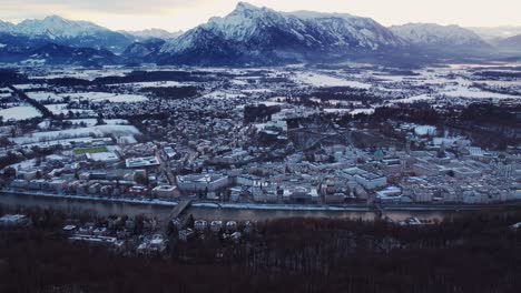 Snow-covered-Fortress-Hohensalzburg-in-Salzburg-with-mountains-behind,-aerial