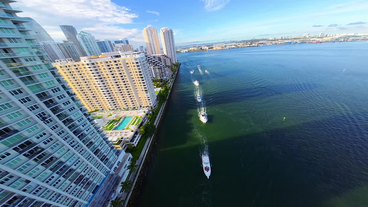 Yachts sail along the waterfront of a modern American city, FPV drone flies above the luxurious buildings in the beautiful residential area.