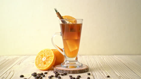 un vaso de café negro americano helado y una capa de jugo de naranja y limón decorado con romero y canela