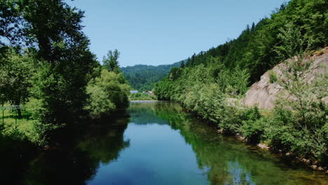 Aerial-view-between-trees-over-river-at-low-altitude,-curved-dolly-in,-Slovenia