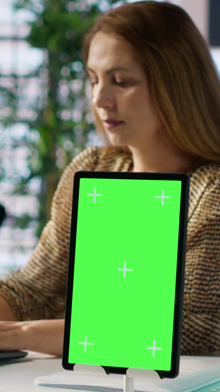 Tablet con display a schermo verde su una scrivania in ufficio, con una donna che lavora.