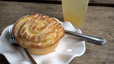 honey glazed roll on a small porcelain plate with knife and fork on the side