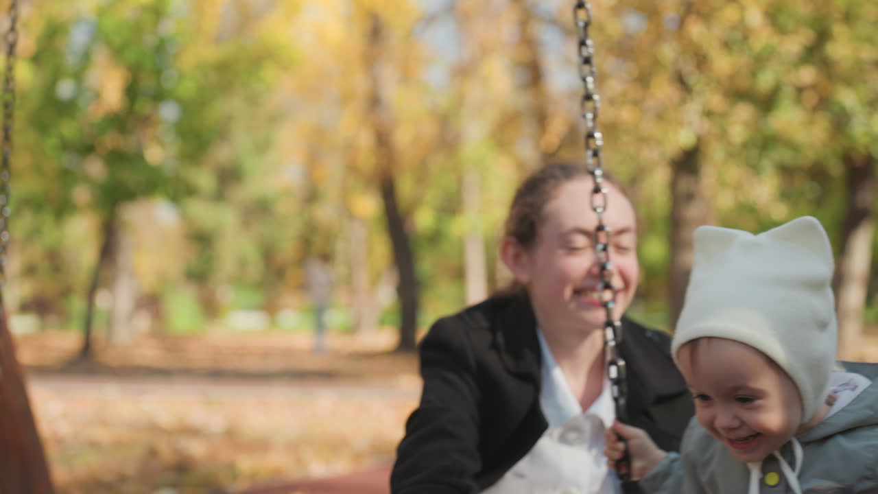 Familieglede deles. Mor og baby koser seg sammen. En gledelig familiescene utendørs med smil. Omsorgsperson og spedbarn fryder seg over lekfull tilknytning under en solrik utendørs familieaktivitet.