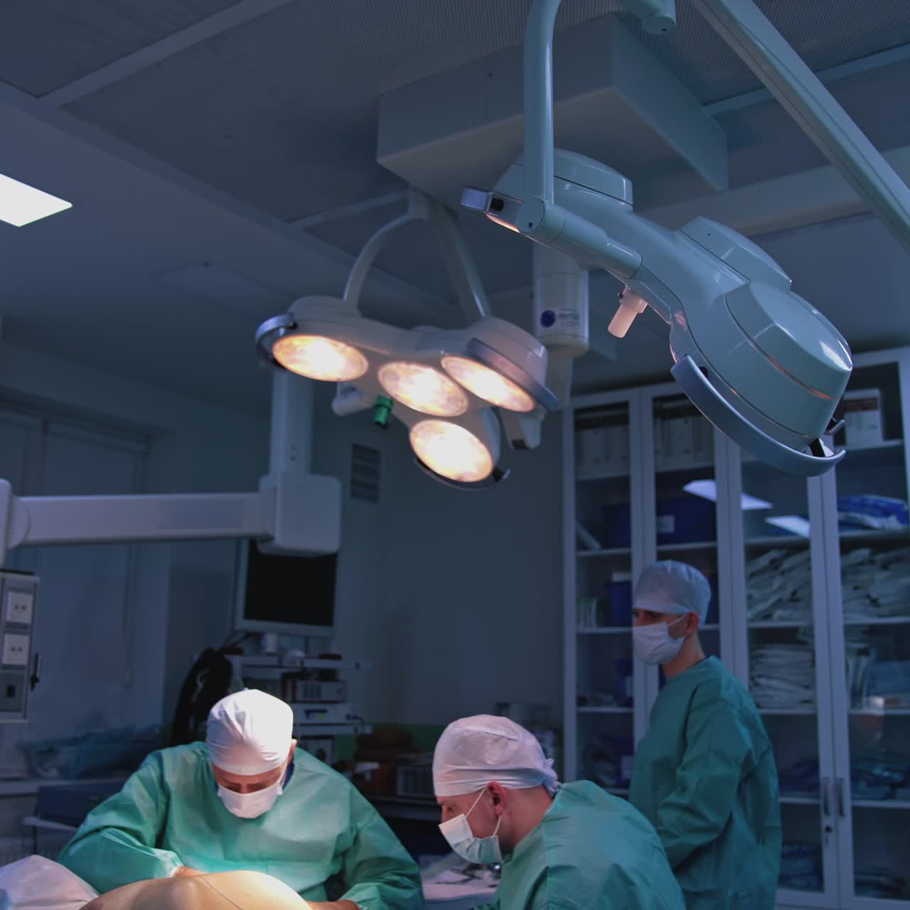 Et team af kirurger udfører en plastikkirurgisk operation på en klinik. Læger i medicinsk maske og uniform opererer en patient under den skarpe lampe i operationsstuen