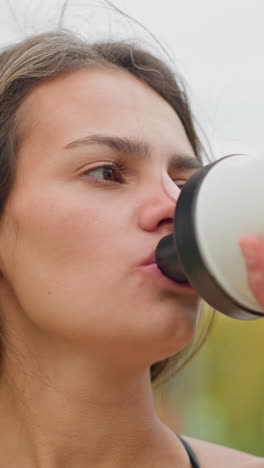 close-up view of an athlete drinking water from black and white water bottle, focusing on hydration and recovery during outdoor workout session, emphasizing fitness and wellness routine