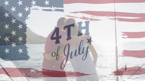 animation of text july 4th with american flag billowing over back view of couple embracing by sea