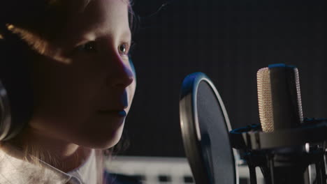 happy child dances in audio studio closeup. pretty little girl smiles near microphone in semi-dark room. kid performs vocal talent in music center