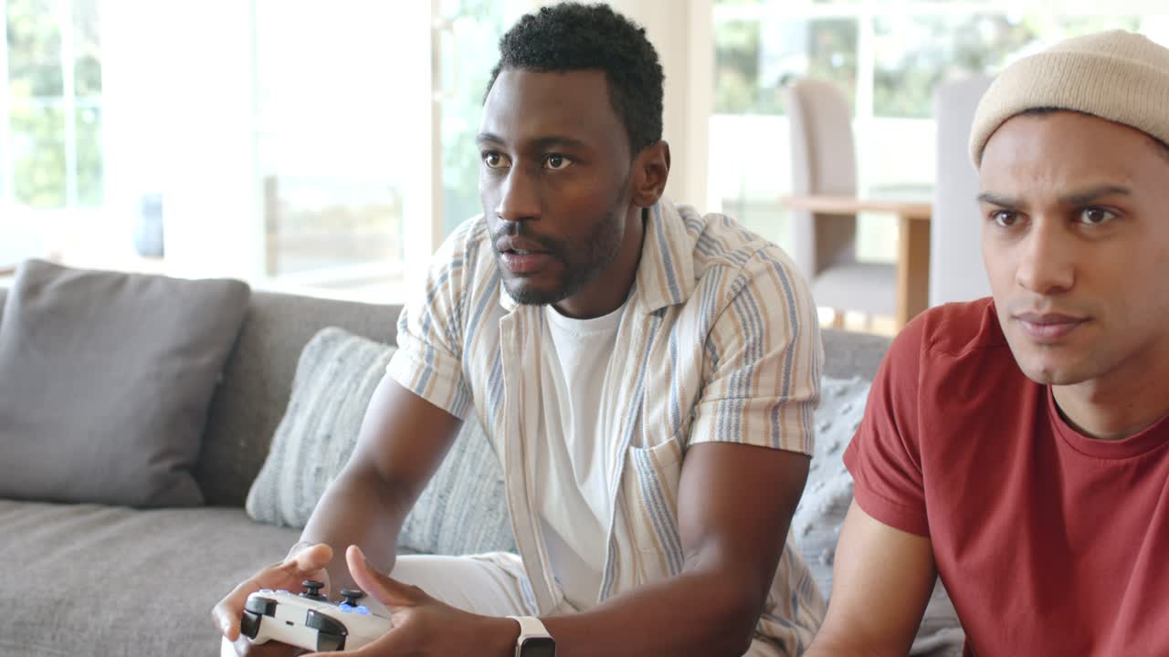 Diversi amici maschi che, seduti su un divano grigio, si sporgono in avanti impugnando i controller e competendo davanti allo schermo