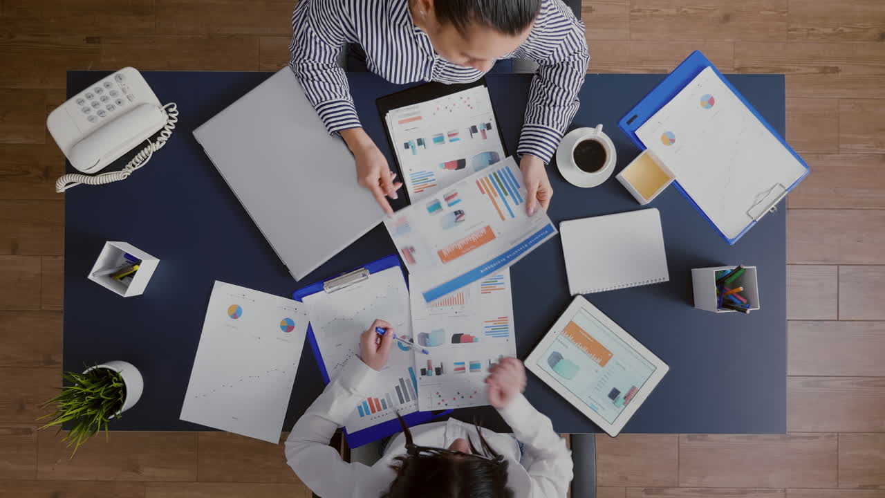 Top view of accountant women analyzing financial graphs paperwork discussing corporate expertise