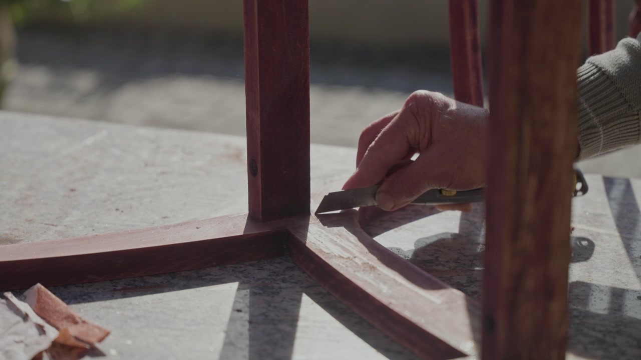 Closeup of hand using small brush to apply stain or varnish to wooden chair leg joint