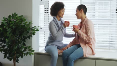 Lesbian-couple-having-coffee-sitting-on-window-sill